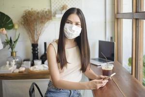 mooie jonge vrouw met gezichtsmasker zit in coffeeshop foto