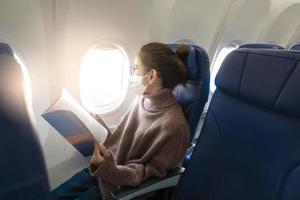 een jonge vrouw met een gezichtsmasker reist met het vliegtuig, nieuw normaal reizen na covid-19 pandemisch concept foto