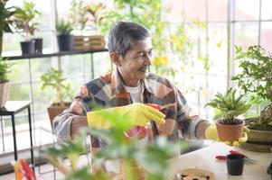 gelukkige senior aziatische gepensioneerde man die boom sproeit en water geeft, geniet thuis van vrijetijdsbesteding