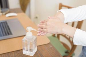 vrouw brengt ontsmettingsgel aan op handen op bureau