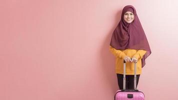 moslimvrouw met hijab houdt bagage op roze achtergrond, mensen reizen concept foto