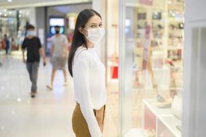 vrouw met beschermend masker winkelen onder covid-19 pandemie in winkelcentrum, protocol voor sociale afstand, nieuw normaal concept.