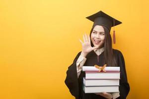 mooie vrouw in afstudeerjurk houdt boeken en certificaat op gele achtergrond foto