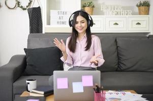 een mooie jonge vrouw die een hoofdtelefoon draagt, voert een videoconferentiegesprek via de computer thuis, een zakelijk technologieconcept. foto