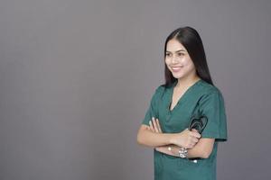 een vrouwelijke arts die een groene scrub en een stethoscoop draagt, is op een grijze achtergrondstudio foto