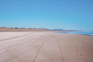 bandenspoor en voetafdrukken markeren op zand met zeegezicht en blauwe lucht foto
