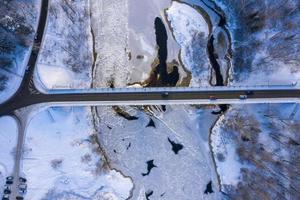 luchtfoto van de rivier en het besneeuwde bos na een sneeuwstorm in een ochtendnevel. heldere blauwe lucht. winter Wonderland. nationaal park gauja, sigulda, letland foto