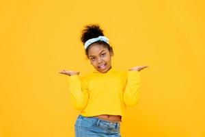 Jonge schattige Afro-Amerikaanse gemengd ras meisje glimlachend en doen open palmen gebaar geïsoleerd op kleurrijke gele achtergrond foto