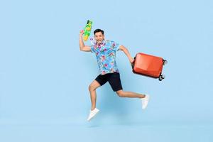springende knappe aziatische toeristenmens die met waterpistool en bagage reist tijdens songkran festival studio schoot blauwe achtergrond foto