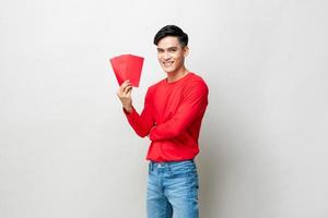 Glimlachende knappe Aziatische man met rode enveloppen of ang pao in studio geïsoleerde grijze achtergrond voor chinees nieuwjaar concepten foto