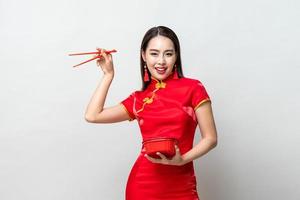 mooie aziatische vrouw in traditionele rode chinese qipao-jurk met plastic voedseldoos en eetstokjes in studio geïsoleerde grijze achtergrond foto