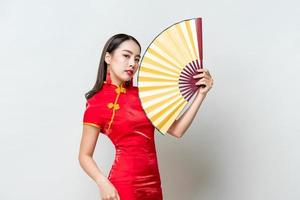 mooie aziatische vrouw, gekleed in traditionele cheongsam qipao jurk met gouden ventilator in geïsoleerde studio lichtgrijze achtergrond voor chinees nieuwjaar concept foto