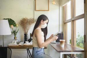 mooie jonge vrouw met gezichtsmasker zit in coffeeshop foto