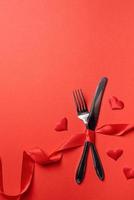 vork en mes vastgebonden met een rood lint in een vorm van hartslag op rode achtergrond foto