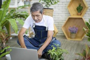 gelukkige senior Aziatische gepensioneerde man met laptop is ontspannen en genieten van vrijetijdsbesteding in de tuin thuis. foto