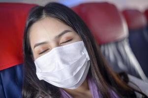 een reizende vrouw draagt een beschermend masker aan boord van het vliegtuig, reist onder covid-19 pandemie, veiligheidsreizen, protocol voor sociale afstand, nieuw normaal reisconcept foto