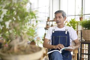 gelukkige senior Aziatische gepensioneerde man lezen en genieten van vrijetijdsbesteding in de tuin thuis.