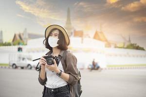 een jonge, mooie aziatische vrouw draagt een beschermend masker dat rond beroemde plaatsen in de stad Bangkok reist, nieuw normaal reizen, covid-19-bescherming, foto