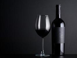 fles rode wijn met een glas op een zwarte achtergrond foto