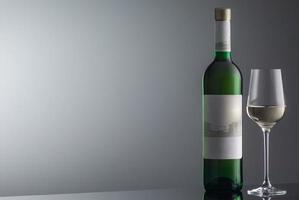 fles witte wijn met wijnglas op grijze achtergrond met verlichting foto