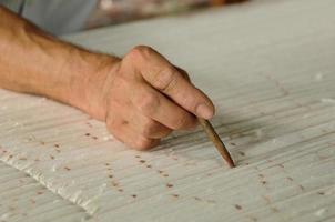 hand met een potlood maakt markeringen op het tapijt. weven en vervaardigen van handgemaakte tapijten close-up foto