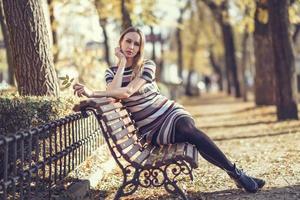 jonge blonde vrouw zittend op een bankje in een park foto