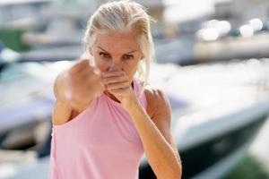 rijpe vrouw die schaduwboksen buitenshuis doet. senior vrouw die sport doet in een kusthaven foto