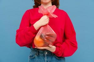 jonge vrouw die rode sweater draagt die plastic vuilniszak houdt foto