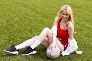 de blondine houdt de bal tussen haar benen op het voetbalveld. foto