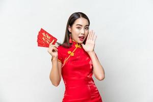 verrast aziatische vrouw in traditioneel oosters kostuum met rode enveloppen of ang pao in grijze geïsoleerde achtergrond, chinese tekst betekent veel geluk grote winst foto