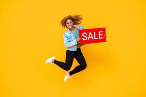 verrast lachende vrouw springen met rode verkoop promotie teken geïsoleerd op gele achtergrond foto