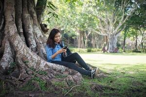 jonge hipstervrouw die op haar telefoon typt terwijl ze in het groene park zit. foto