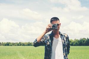 jonge hipster knappe man fotografie staande retro camera schieten met natuur genieten en gelukkig op grasland. foto