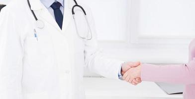 hand van dokter schudt vrouwelijke arm zijn patiënt in kliniek, medisch kantoor. zorgconcept, zorgverzekering foto