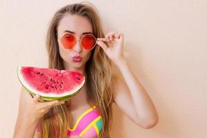 close-up van gelukkig meisje in roze zonnebril en watermeloen fruit. zomervakantie en leuke tijd weekend. zomer concept. lachende jonge vrouw in mode zwembroek. selectieve aandacht. strand zomer outfit. foto