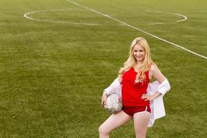 blonde met een bal op het voetbalveld in rood uniform. foto