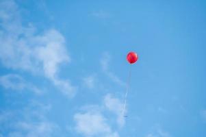 een rode ballon die onder de blauwe lucht en witte wolken vliegt foto