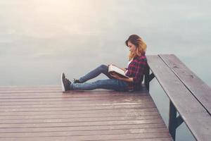jonge mooie hipster vrouw ontspannen zittend op de pier leesboek. foto