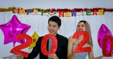 Aziatische koppelliefhebber met 2020-nummers die een nieuw jaar vieren in een bar, schreeuwend en lachend en aftellend tot middernacht op een nieuwjaarsfeest foto