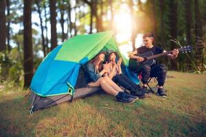 een groep Aziatische vrienden die in de zomer samen met geluk gitaar drinken en gitaar spelen tijdens het kamperen foto