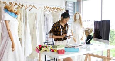 klein bedrijf van aziatische modeontwerper die werkt en een smartphone en tablet gebruikt met trouwjurken in de kledingwinkel foto