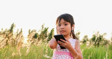 Aziatisch kindmeisje dat naar muziek luistert en zingt vanaf een mobiele telefoon en gelukkig is op de weide in de zomer in de natuur foto