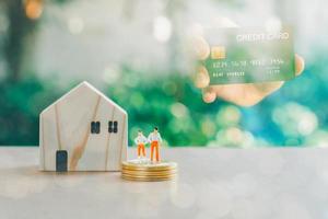 zakelijke en financiële concept. dubbele belichting hand met creditcard en houten huis met kleine mensen model staan op een stapel gouden munten. foto