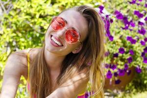 zomervakanties. close-up vrouw blij gezicht in roze zonnebril op tuin achtergrond. zomers leuk weekend. mooi meisje met een perfecte witte tandenglimlach. selectieve aandacht. strand outfit foto