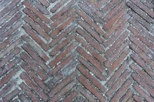 bemost diagonaal patroon van baksteenbestrating in een visgraatstijl voor achtergrond, oude oranje bakstenen tegelvloer met zigzagpatroon. oude peeling chevron zigzag diagonale metselwerk textuur achtergrond. foto