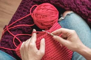 handen vrouw in een gezellige thuisomgeving breit van een roze draad. bovenaanzicht. kopiëren, lege ruimte voor tekst foto