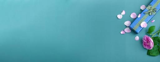lange blauwe geschenkdoos met een theeroos op een turquoise achtergrond. vakantie geschenken close-up met kopie ruimte foto