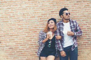 portret van jonge hipster paar poseren met haar vriendje met een kopje koffie samen genieten van vakantie tegen bakstenen muur achtergrond. foto