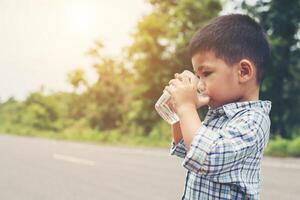 kleine schattige aziatische jongen drinkwater uit de glazen langs de weg, moe om te spelen. foto