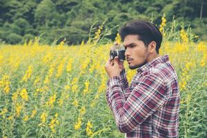 jonge knappe hipster man fotograferen met retro camera met gele bloem natuurveld. foto